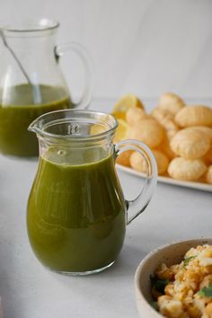 there is a pitcher of green liquid next to two bowls of food on the table