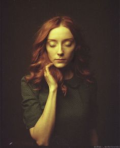 a woman with long red hair is posing for a photo in front of a black background