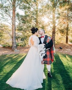 a bride and groom kissing in the grass at their scottish themed wedding ceremony, with trees in the background