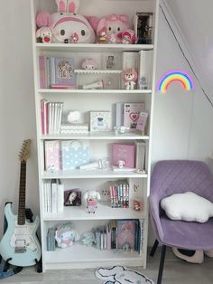 a white book shelf filled with lots of books next to a purple chair and guitar