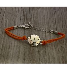 a basketball bracelet with an orange cord and silver ball on the front, sitting on a wooden surface