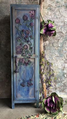 an old door with flowers painted on it next to a tree branch and rugs