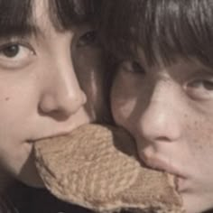 two people with long hair and one has a large piece of food in his mouth