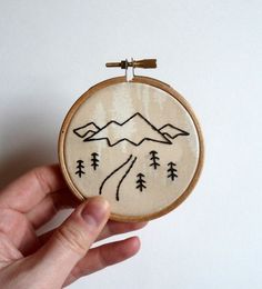 a hand holding a small embroidered ornament with mountains and trees on it