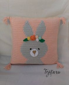 a crocheted bunny pillow with flowers on it's head and tassels around the ears