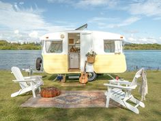 an old camper is parked on the grass near some chairs and a picnic table