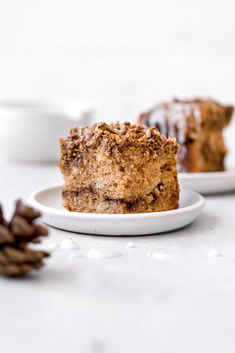 two pieces of cake sitting on plates next to some pine cones and cinnamon sticks in the background