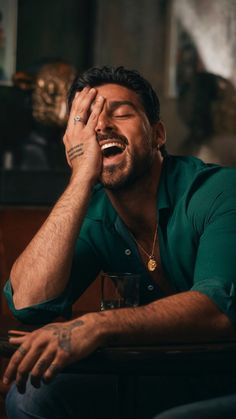 a man sitting at a table with his eyes closed and hands on his face while holding a glass in front of him