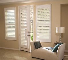 a living room filled with furniture and windows covered in white shutters, next to a lamp