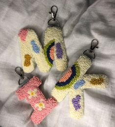 three crocheted keychains sitting on top of a white bed covered in sheets