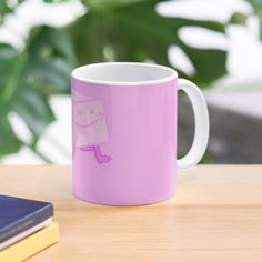 a pink coffee mug sitting on top of a wooden table next to a laptop computer