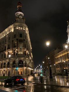 a very tall building sitting on the side of a wet street at night with traffic passing by