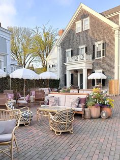 an outdoor patio with wicker furniture and umbrellas in front of a large house