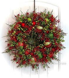 a christmas wreath hanging on the front door with red and green balls, greenery and baubles