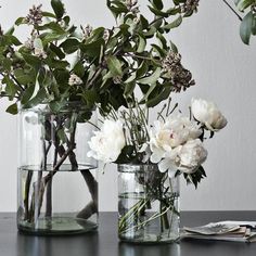 two glass vases with flowers in them sitting on a table next to each other