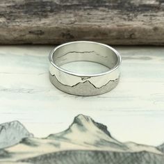 a silver ring sitting on top of a piece of wood next to a mountain range