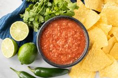 a bowl of salsa surrounded by chips and limes