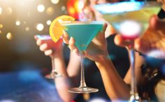 people holding up colorful cocktails at a party stock photo