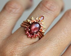 a woman's hand with a red ring on top of her finger and an orange stone in the middle