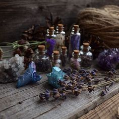 bottles filled with different types of crystals and herbs on a wooden table next to twine of twine needles