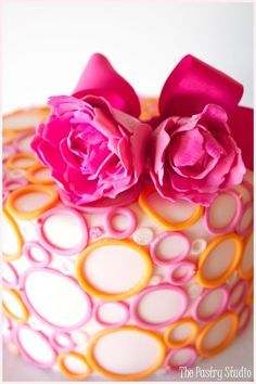 a close up of a decorated cake with pink flowers on top and orange circles around it