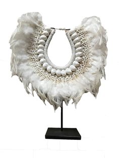 a white necklace on a black stand with beads and feathers hanging from it's neck