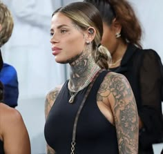 a woman with tattoos on her neck and chest standing in front of other women wearing black dresses