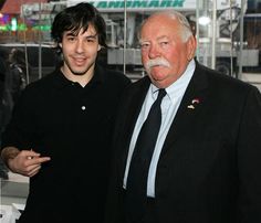 two men standing next to each other in front of a glass wall with an american flag on it