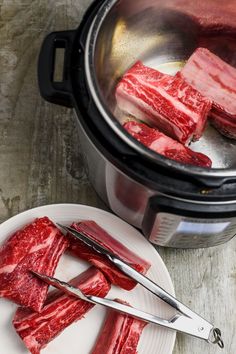 raw meat being cut into cubes in front of an open crock pot with tongs