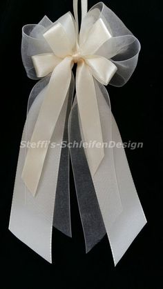 a white and grey ribbon with a bow on the top is hanging from a black background