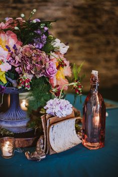 an arrangement of flowers, candles and books on a blue table cloth with a bottle