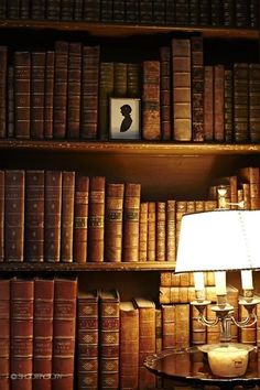 a lamp on a table in front of a bookshelf filled with old books