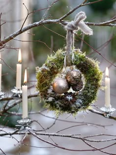 an ornament hanging from a tree with candles in the foreground and snow on the ground