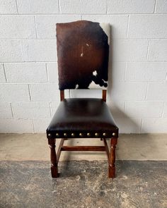 a brown leather chair sitting in front of a white brick wall with studded wooden legs