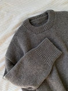 a gray sweater laying on top of a bed next to a white pillow and blanket