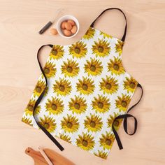 an apron with sunflowers on it next to eggs and wooden utensils