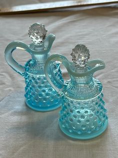 two blue glass vases sitting on top of a white cloth covered tablecloth,