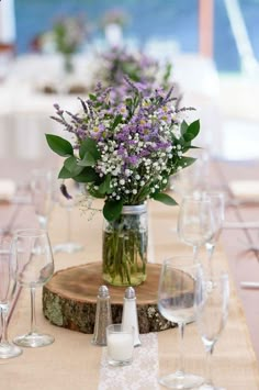 there is a vase with flowers in it on top of a wooden table surrounded by wine glasses