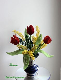 a vase filled with red flowers on top of a white table next to a wall