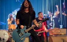 a man with long hair and beard playing an electric guitar in front of other musicians