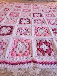 a pink and white crocheted blanket sitting on top of a bed