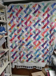 a colorful quilt hanging from the side of a wall in a room with shelves and shelving