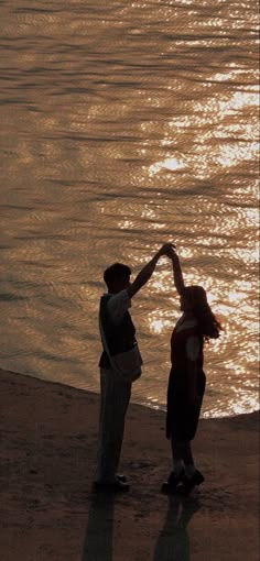 two people are standing on the beach and reaching out to touch each other's hand