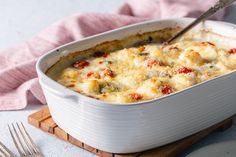 a casserole dish with cheese and vegetables in it on a cutting board next to a pink towel