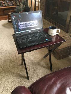 a laptop computer sitting on top of a wooden table next to a leather couch in front of a fireplace