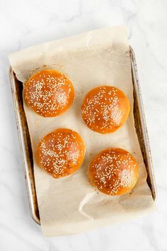 four buns with sesame sprinkled on them in a baking tin, ready to go into the oven