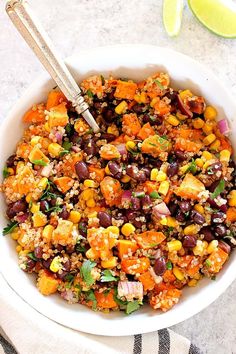 a bowl filled with black beans, corn and cilantro next to a lime wedge