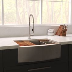 a stainless steel kitchen sink in front of a window with white walls and counter tops