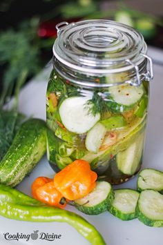 pickles and cucumbers sit in a jar on a table next to other vegetables