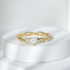 a gold ring with a heart shaped diamond in the middle on top of a white surface